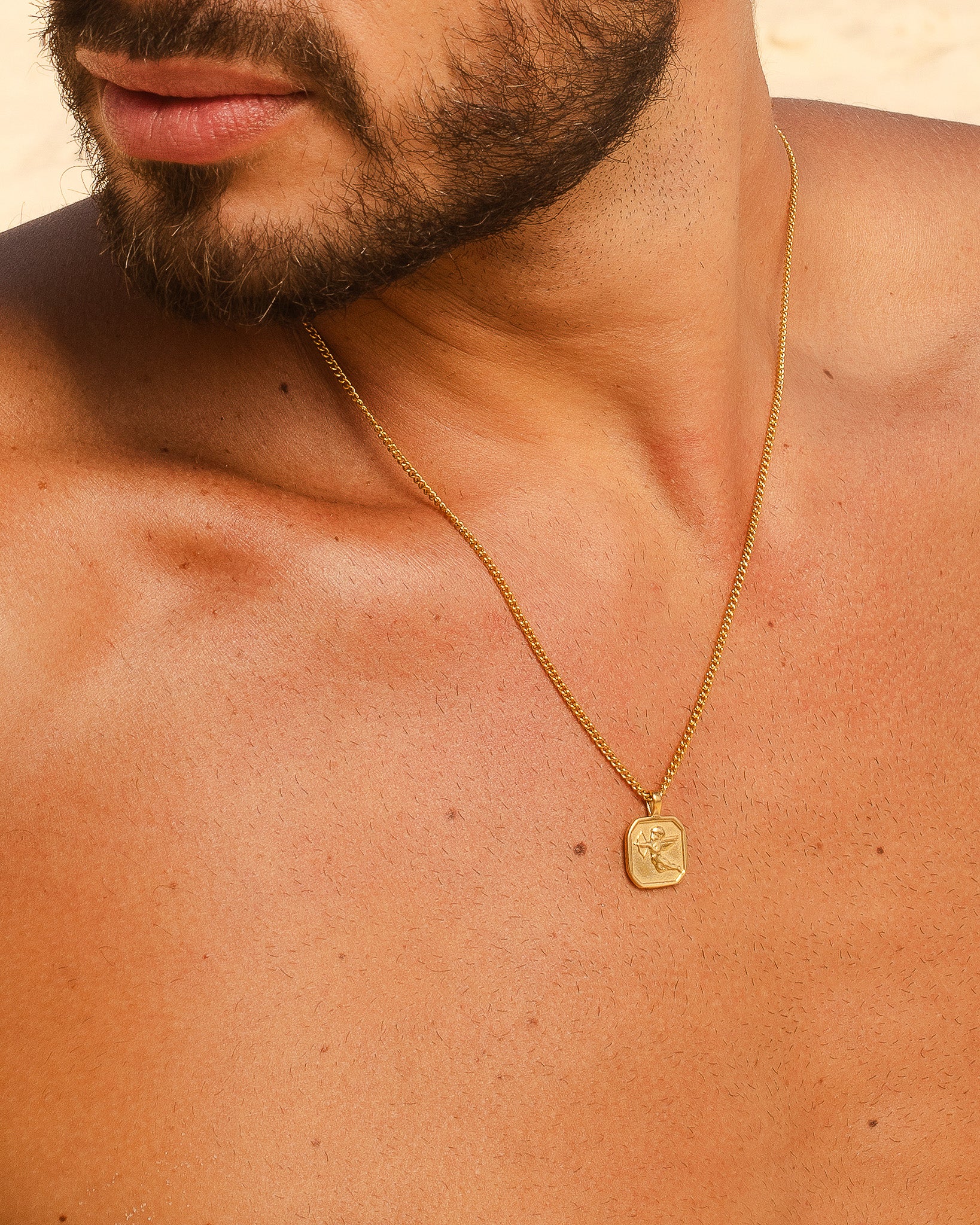 Gold chain necklace with a square pendant displaying an emblem resting on the man’s chest.