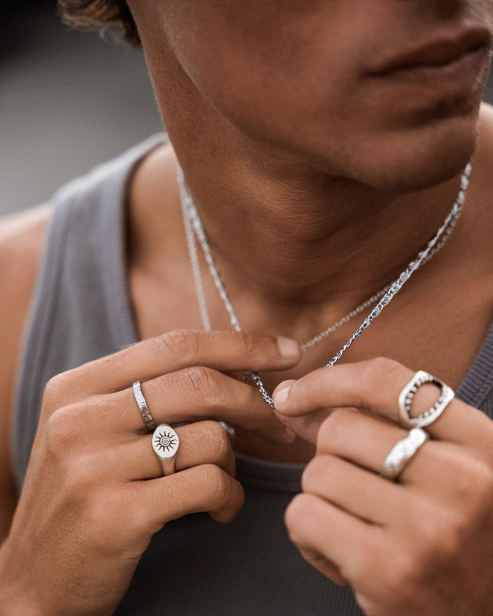 Energy silver ring with a sunburst disc worn on the finger, silver chains visible in the background.