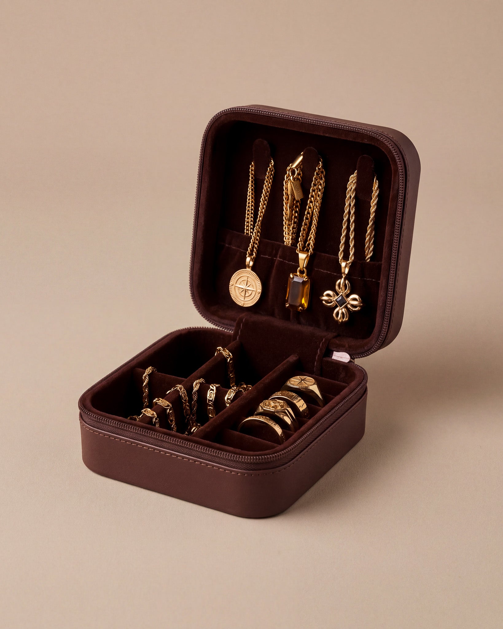Geöffnete bordeauxrote Schmuck-Reisebox mit Goldketten und Anhängern